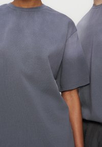 Δύο άτομα που φορούν απλά γκρι κοντομάνικα μπλουζάκια με στρογγυλή λαιμόκοψη, σε κάδρο που απεικονίζει το πάνω μέρος του κορμού και μέρος από ένα χέρι.