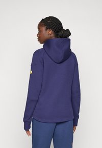 Marineblauer Hoodie mit Kordelzugkapuze, Kängurutasche und gelbem Logodetail am Ärmel. Hergestellt aus einem weichen, strukturierten Baumwollmischgewebe.