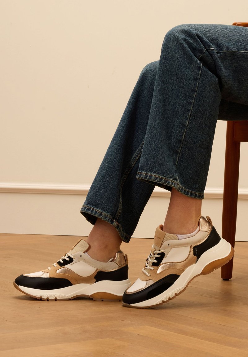 Sneaker chunky con un mix di materiali beige, neri e bianchi, caratterizzati da dettagli testurizzati e una suola imbottita per il comfort.