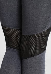 Legginsy o wysokim stanie w ciemnoszarym kolorze z teksturowaną czarną siateczką, z kontrastowym wzorem w kolorowe bloki na nogawkach.