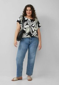 Schwarz-weiß geblümte Bluse mit kurzen Ärmeln, kombiniert mit hellblauen geraden Jeans und beigen Rutschen.