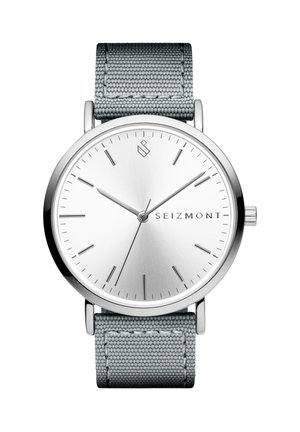 Sølv rund klokke med minimalistisk urskive, sølv timeindikatorer, grå stoffreim og merkenavnet "SEIZMONT" på urskiven.