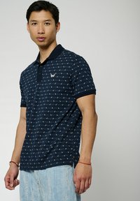 Polo shirt blu navy con un motivo testurizzato e un piccolo logo ricamato. Presenta un colletto classico e una chiusura a tre bottoni.