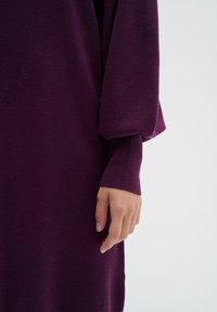 Lila stickad klänning med en avslappnad passform, puffärmar och åtsittande manschetter som visar textur och tygstruktur.