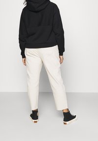 Sudadera con capucha negra, pantalones recortados beige claros, zapatillas de deporte negras de caña alta con suelas blancas, detalles mínimos, texturas lisas.