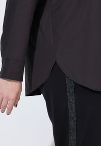 Sort langærmet skjorte med buet kant og knapmanchetter, lavet af et glat materiale. Et sorte bukser med en glitrende lodret stribe på siden.