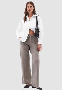 Camicia bianca con bottoni, pantaloni larghi a righe grigie con vita regolabile, e ballerine nere. Il modello tiene anche una piccola borsa nera.