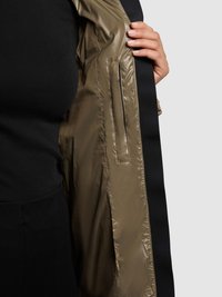 Chaqueta de nailon verde oliva con textura lisa, que presenta un ribete negro y un bolsillo interior con cremallera. El interior muestra un acabado brillante.