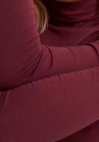 Burgundy pitkähihaineen poolopaita, joka on valmistettu pehmeästä kankaasta. Mallissa on istuva muotoilu ja sileä rakenne, jossa on näkyvät saumat.