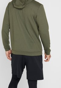 Sweat-shirt vert olive avec capuche et manches longues, associé à un short de sport noir. Poignets et ourlet côtelés, texture douce.