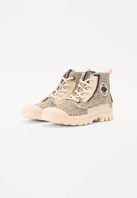 Zapatillas de caña alta de color beige claro con un patrón de manchas, suela de goma, cordones en la parte delantera y una etiqueta de acento naranja; presenta un logo en el costado.
