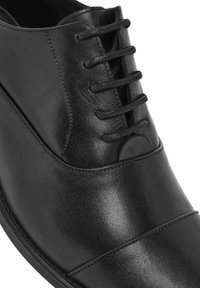 Chaussure de ville en cuir noir avec une texture lisse, une forme structurée, un laçage sur le devant et des détails de coutures horizontales subtils.
