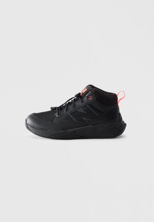 Black mid-top athletic shoe with textured sole, mesh and leather upper, elastic laces, and red pull tab at heel on plain background.