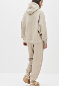 Béžová oversized mikina a ladící tepláky, se elastickými manžetami a texturovaným lemem, doplněné koženými slip-on botami s kožešinovou podšívkou.
