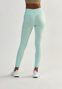 Miętowe legginsy z wysokim stanem, z kieszonką po boku i fakturowanym materiałem. Zestawione z białymi butami sportowymi.