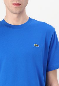 Μπλε βαμβακερό T-shirt με στρογγυλή λαιμόκοψη, που διαθέτει ένα μικρό κεντητό πράσινο λογότυπο κροκόδειλου στο αριστερό στήθος. Λείο υλικό.