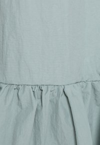 Lichtblauwe katoenen jurk met een geplooide ruffle zoom en een textuurafwerking, met een gladde, licht gekreukte uitstraling.