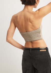 Beez värvi lühike bandeau-top, millel on smockitud tekstuur; sobitatud kõrge vöökohtadega tumedat denimi teksadega, millel on kaks tagakotti ja nahkdetailid.