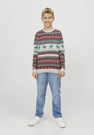 Gebreide trui met een rood, groen en crèmekleurig patroon met rendiermotieven. Gepaard met lichtblauwe jeans en witte sneakers.