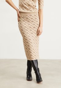 Gonna beige in maglia con un motivo testurizzato di piccole forme marrone scuro; abbinata a alti stivali in pelle nera.