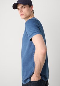 T-shirt κοντομάνικο με στρογγυλή λαιμόκοψη σε ομοιόμορφο μπλε χρώμα. Φτιαγμένο από μαλακό βαμβάκι, με ορατές ραφές και άνετη εφαρμογή. Συνδυασμένο με σκούρα τζιν.