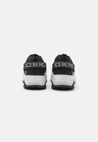Czarno-białe trampki na masywnej podeszwie, z fakturowaną cholewką i wyraźnym paskiem z logo „ICEBERG”. Widok z tyłu pokazuje wyściełany kołnierz.