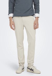 Pantaloni color crema con vestibilità slim, realizzati in tessuto elasticizzato, caratterizzati da una texture liscia e senza elementi metallici o fantasie visibili.