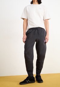 Ljusbeige bomulls-t-shirt med korta ärmar och en liten logotyp på bröstet, i kombination med mörkgrå sweatpants med elastisk midja.