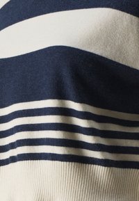 Pull rayé bleu marine et crème avec de larges rayures horizontales et un ourlet côtelé. Texture douce avec une finition lisse.