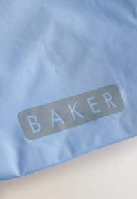 Ljust blått tyg med ordet "BAKER" tryckt i grå blockbokstäver inuti en rundad rektangel nära nederkanten.
