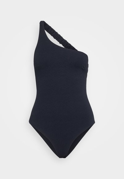 Vienvirsmas peldkostīms tumši zils, ar teksturētu audumu un viļņotu siksniņu. Klasiķa siluets ar augstiem griezumiem kājstarpē.