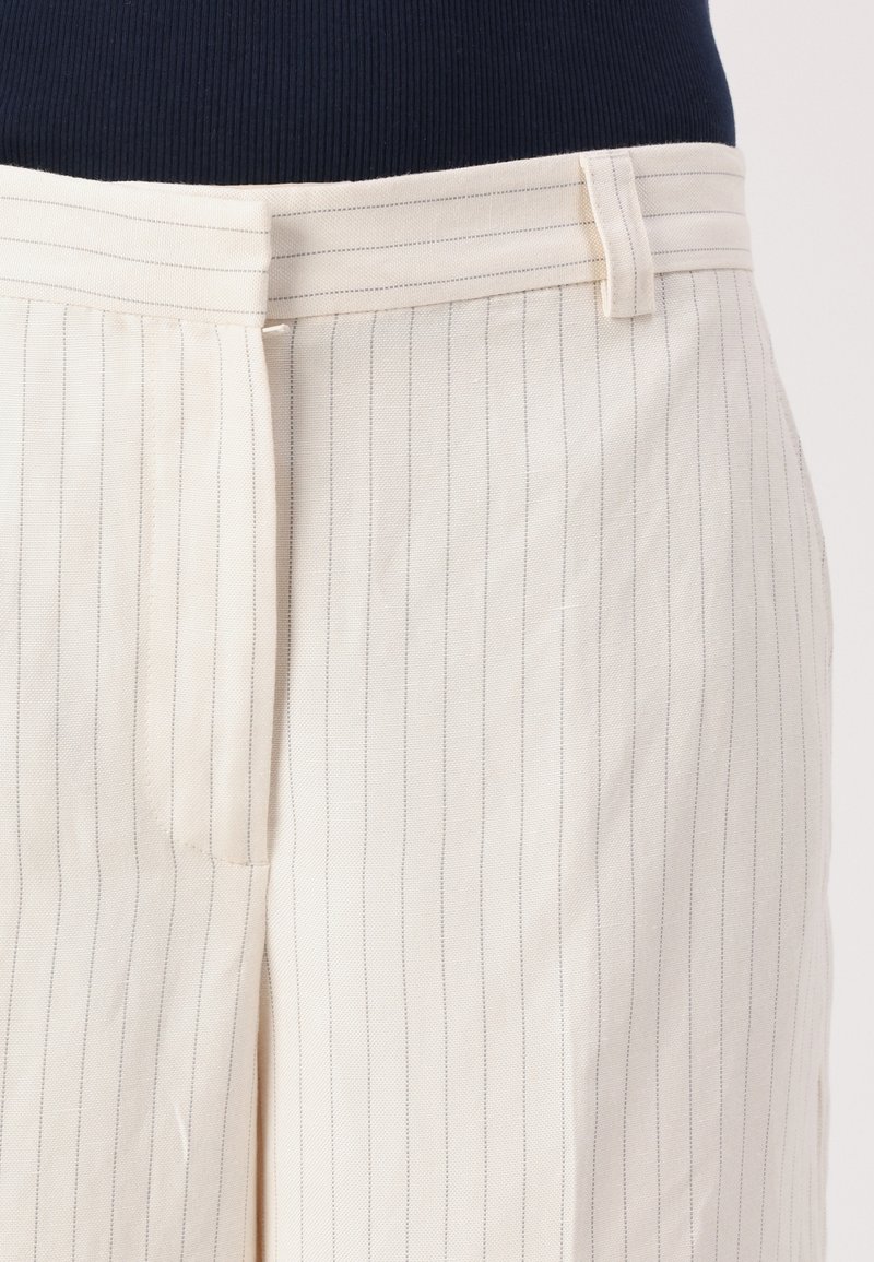 Beżowe spodnie w paski wykonane z lekkiego materiału, z prostym krojem, szlufkami na pasek oraz pionowymi paskami w kontrastującym kolorze.