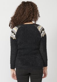Pull noir en matière douce et pelucheuse, avec des accents tricotés à motifs sur les épaules en zigzags gris, or et blanc.