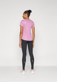 Aansluitend roze shirt met korte mouwen, gecombineerd met zwarte leggings. De leggings hebben accentdetails bij de enkels en lichtgekleurde sneakers.