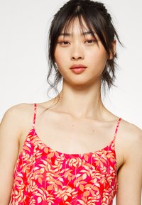 Vestido floral de alças em rosa vibrante com padrões de folhas laranja e brancas. Tecido leve com um corte relaxado e textura suave.