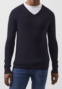 Granatowy sweter w serek, długi rękaw, prążkowane mankiety i dół, lekka tkanina, nałożony na biały sweter z okrągłym dekoltem, casualowy krój.