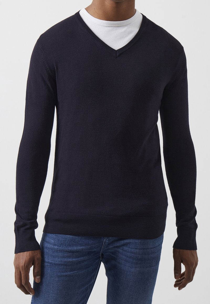 Granatowy sweter w serek, długi rękaw, prążkowane mankiety i dół, lekka tkanina, nałożony na biały sweter z okrągłym dekoltem, casualowy krój.