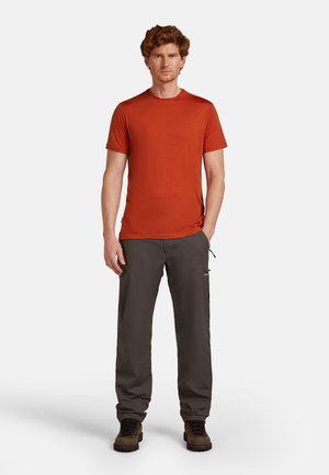 Rotes T-Shirt mit kurzen Ärmeln und Rundhalsausschnitt, kombiniert mit einer dunkelgrauen Hose, die seitliche Taschen und eine lockere Passform hat.