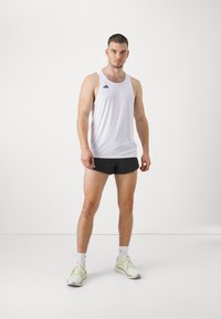 Hvid ærmeløs tanktop med sort Adidas-logo, parret med sorte shorts og lysfarvede træningssko. Rent, minimalistisk design.