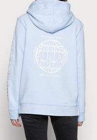 Jasnoniebieska bluza z kapturem, z białym napisem i ilustracją na plecach. Na jednym z rękawów nadrukowany napis "RAZEM OSIĄGAMY SUKCES".