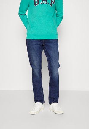 Felpa con cappuccio turchese con logo "GAP", abbinata a jeans blu scuro e sneakers bianche. La felpa ha una tasca a canguro e una vestibilità casual.