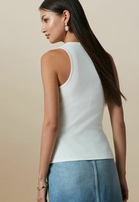 Hvid ribbet tanktop med en tætsiddende pasform, med rund halsudskæring og uden ærmer, parret med en lyseblå denimnederdel.