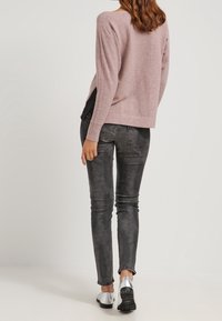 Ljusrosa tröja med ribbade muddar och nederkant, parat med slim-fit, blekta svarta jeans och silverfärgade lägenheter, sedd bakifrån.