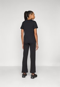 T-shirt nera in cotone con maniche corte, abbinata a pantaloni neri a zampa d'elefante e sneakers nere. Design semplice con una texture liscia.