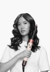 Locktång med en rosa och svart design, texturerad kropp och ett unikt ansiktsmönster. Modell som håller i tången, if örd en vit topp och med svart hår.