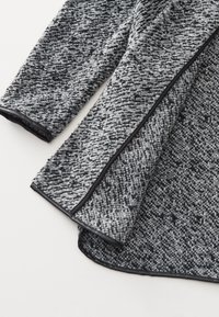Vêtement à manches longues tricoté gris et noir avec un motif texturé et un passepoil noir le long des bords.