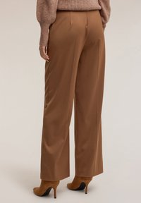 Ruskeat leveälahkeiset housut sileästä kankaasta, joissa korkea vyötärö ja siistit linjat. Yhdistetty vaaleanpunaiseen tekstuuriin neuleeseen ja korkokenkään.