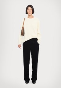 Pull en côtes crème, pantalon noir ajusté et chaussures noires. Sac marron avec une fine bandoulière. Design simple, texture lisse.
