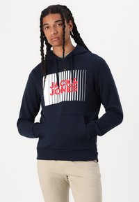 Felpa navy con grafica "JACK & JONES" in bianco e rosso, caratterizzata da linee orizzontali. Realizzata in tessuto morbido, con tasca a marsupio e polsini a costine.