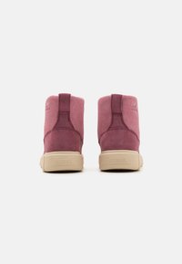 Rosa semsket ankelstøvler med en strukturert overflate, med en beige gummisåle og bakre trektab, merket med "SOREL"-merking.